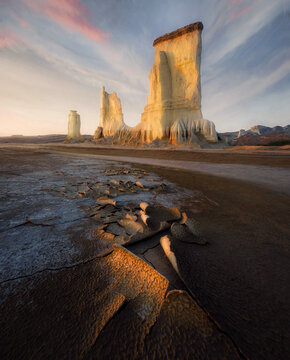 View of majestic white rock pillars standing in a vast desert with parched cracked ground under a colorful sunset sky Balochistan, Pakistan.