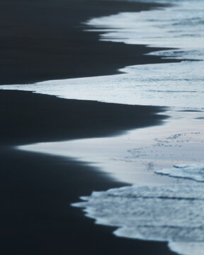 View of gentle waves washing over dark sand along the shoreline in Balochistan, Pakistan.