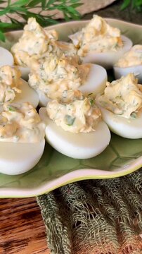 Vertical close-up of homemade deviled eggs with chunky creamy herb filling on a patterned plate, highlighting classic appetizer texture and fresh party food presentation.