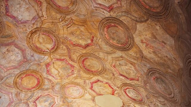 Detailed Pompeii ceiling fresco with circular medallions and geometric painted motifs, showing richly ornamented Roman vault decoration inside an ancient room.