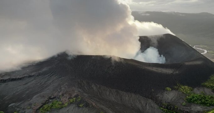 Close up view of Mount Yasur, an active volcano on Tanna Island, Vanuatu, erupting and releasing thick plumes of smoke and ash from its caldera, raw natural power and geology. Zoom out drone flight