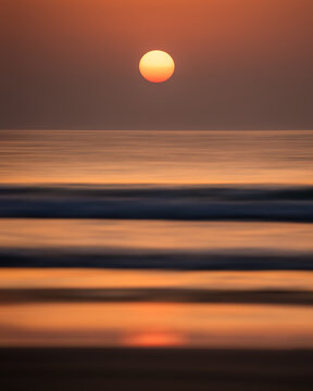View of the sun setting over the calm ocean with soft waves and orange reflections on the water in Balochistan, Pakistan.