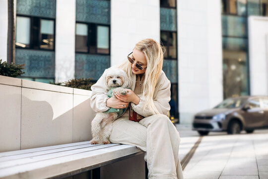 Woman with Maltese dog on city bench, stylish urban lifestyle