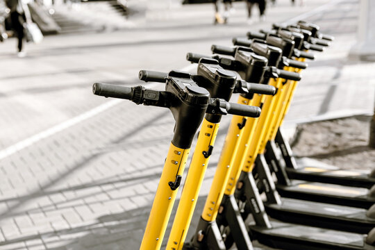 Yellow electric scooters lined up in city street, urban eco transport concept.