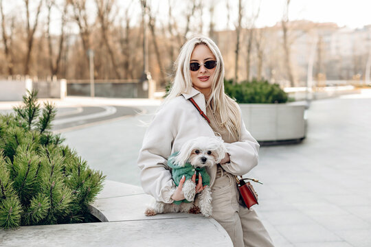 Fashion woman with cute small Maltese dog sitting outdoors, urban lifestyle