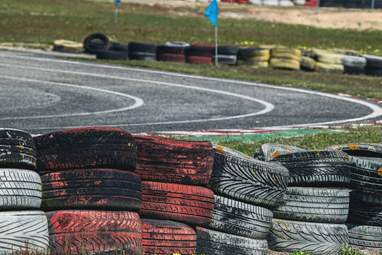 View of a racing track with a barrier of weathered stacked tires painted red, white and black in the foreground and asphalt curves.