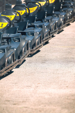 View of a row of black go-karts with yellow numbers parked on an asphalt racing track under bright sunlight.