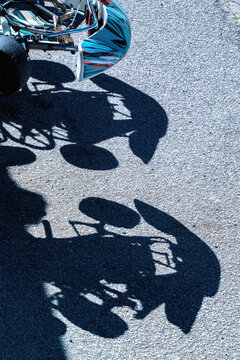 View of the shadow of a go-kart and driver cast on grey asphalt under bright sunlight.