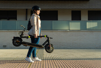 Woman carrying folding electric scooter in city street © ALIDA