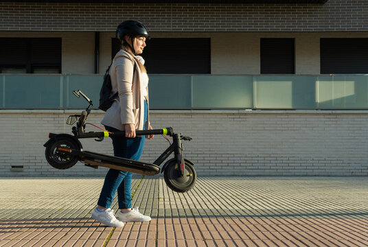 Woman carrying folding electric scooter in city street