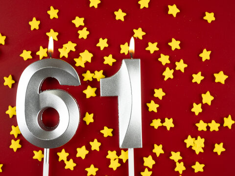 Number 61 silver celebration birthday candle on red with golden stars background. Sixty-one years birthday. celebrating anniversary and birthday