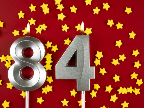 Number 84 silver celebration birthday candle on red with golden stars background. Eighty-four years birthday. celebrating anniversary and birthday