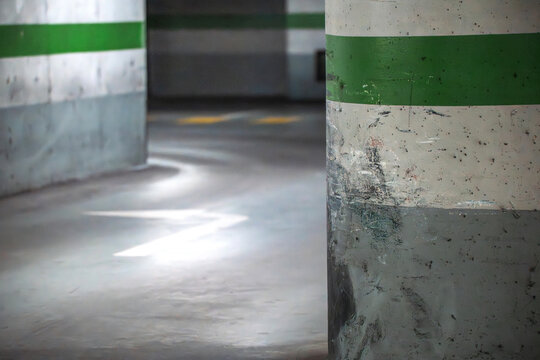 View of a scratched concrete pillar with a green stripe in an empty underground parking garage with painted arrows on the floor.