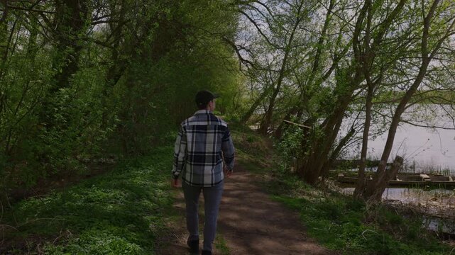 Young man in a plaid shirt strolling through a green spring park, slow motion