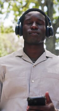 Black man, typing and happy at park with headphones, streaming or listen to music on commute. African person, smile and travel inspiration with thinking, mobile app or audio subscription in town