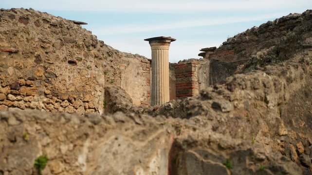 View across layered Pompeii ruins with a standing fluted Roman column framed by weathered stone walls and brickwork inside the ancient archaeological site.