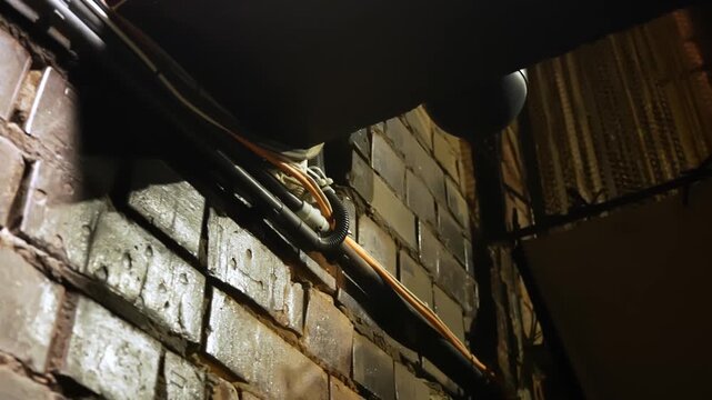 Warm backstage close-up of exposed electric cables and conduits running along a brick wall, revealing technical theater infrastructure and hidden stage utility systems.