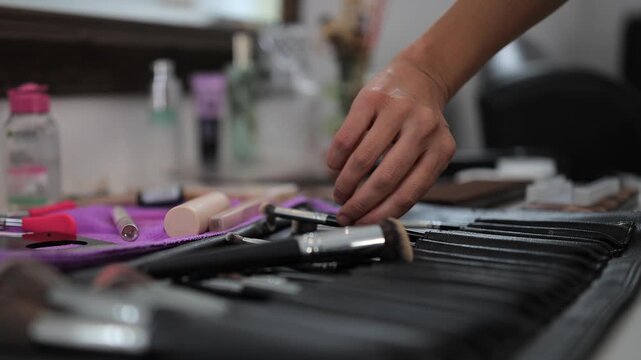 Woman's hand picks makeup brush from aesthetics kit on counter top