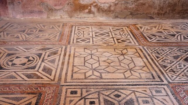 Wide view of preserved mosaic flooring in Pompeii, showing intricate Roman geometric patterns, earthy tones, and ancient decorative design inside a historic interior.