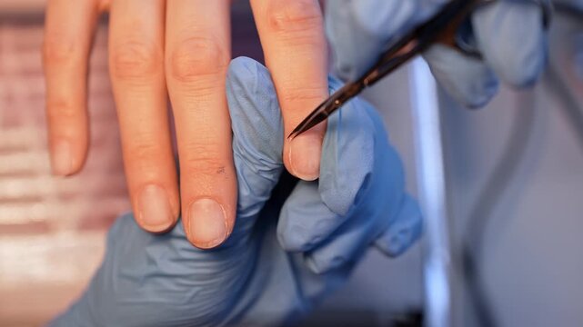 Precision salon close-up of a manicurist trimming the cuticle area with fine scissors during dry manicure prep, showing hygienic detail work and careful professional nail care.
