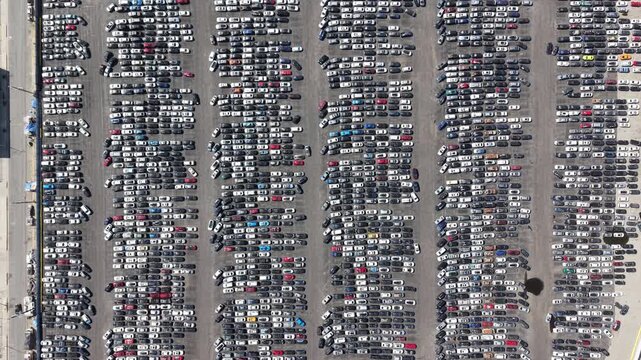 Cinematic daytime aerial drone footage captured from a high bird&rsquo;s-eye perspective in Los Angeles, featuring a smooth reverse dolly pulling away from a dense urban car junkyard.