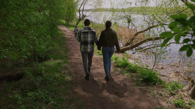 Back view of a happy family walking along a forest path by the lake, slow motion