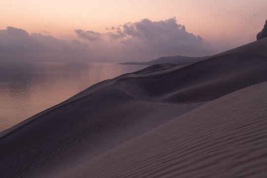 View of sand dunes overlooking the sea under a soft pink sunset sky with scattered clouds Socotra, Yemen.