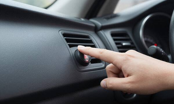 driver hand reaches press hazard warning flasher button vehicle dashboard shot soft overhead natural