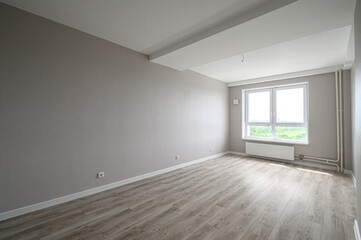 Fototapeta premium spacious, empty room with light grey walls, wooden laminate flooring, large double window, white radiator, recessed ceiling, minimal fixtures, natural light, neutral palette