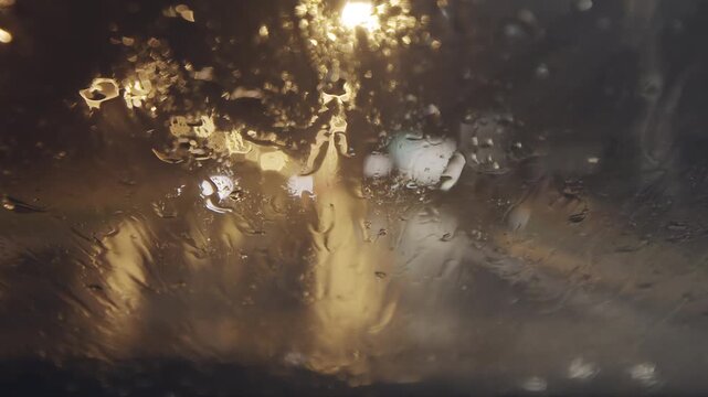 Car windshield with raindrops and blurred city lights captured in moody urban driving perspective