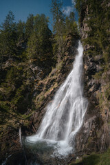 Obraz premium Powerful waterfall cascading down a rocky forest cliff in an alpine landscape in Tyrol, Austria.