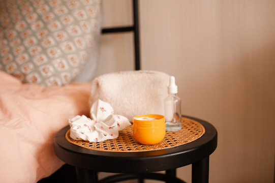 Body lotion jar with makeup bag and scrunchy on bed rattan table in bedroom. Cozy home interior.