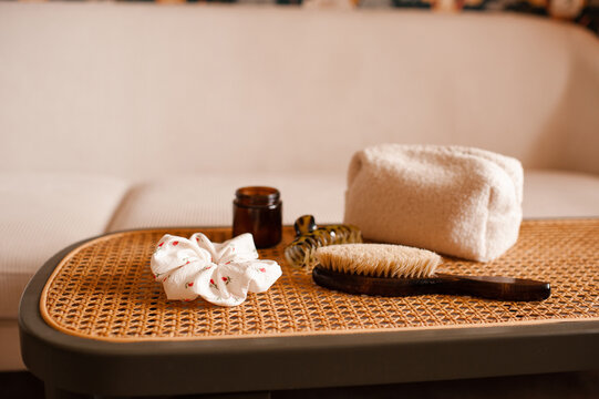 Hair accessories: natural brush, scrunchy, hair clip and makeup bag on rattan table over couch in living room. Cozy domestic interior.
