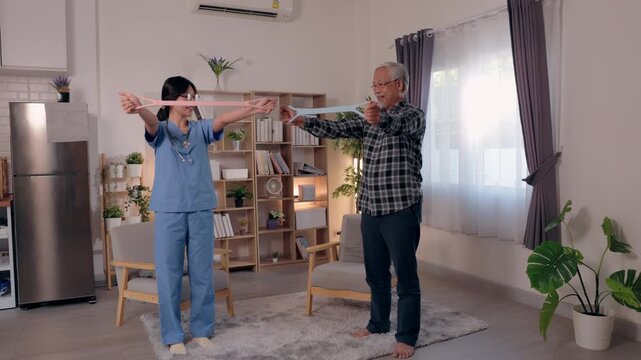 Nurse caregiver guiding senior man with resistance band exercise at home for physiotherapy rehabilitation, standing and arm stretch physical therapy in living room to improve mobility and balance