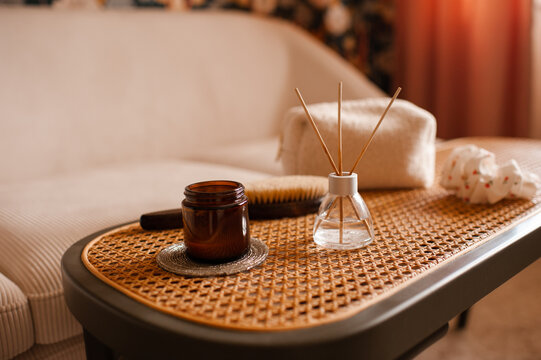Cozy home atmosphere with liquid home perfume in glass bottle and sticks with candles on rattan table with couch in living room. Hygge domestic interior.