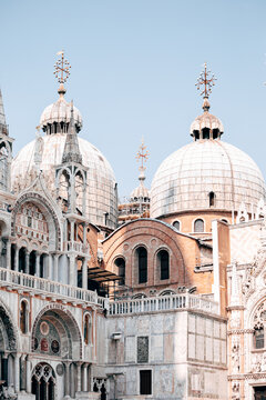View of the ornate Byzantine domes and marble facade of Saint Mark's Basilica under a clear blue sky in Venice, Veneto, Italy.