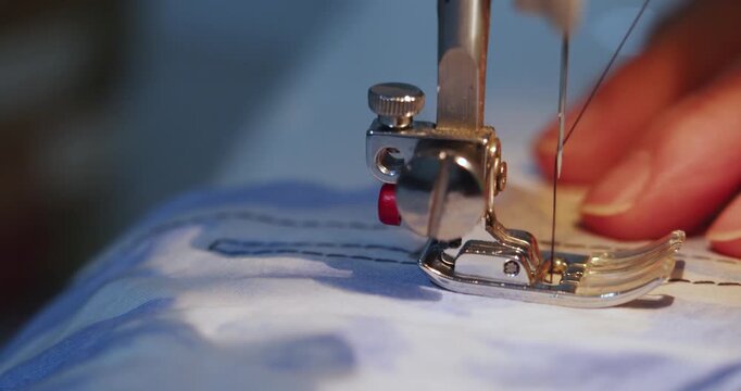 Close-up of hands skillfully sewing blue fabric with a machine. The precise stitching highlights craftsmanship and focus as the fabric flows smoothly under the needle. 60 fps 4k footage.