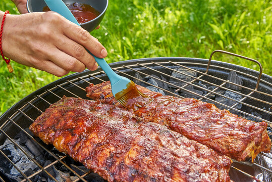 Grilled ribs celebration. Preparing and basting juicy pork ribs during relaxed outdoor summer barbecue