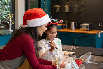 Indian female mother-daughter with Santa hat and antlers mixing batter at kitchen island with whisk © wavebreak3