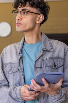 Male wearing denim jacket and tortoiseshell glasses, holding tablet with blue-gray case in lounge