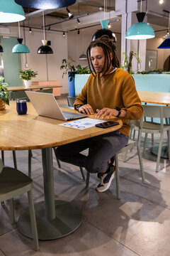African American man working on laptop at coworking cafe, reviewing color chart and smartphone
