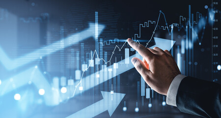 Obraz premium Business hand interacting with rising financial graphs and glowing market indicators showing growth trend on futuristic blue digital background.