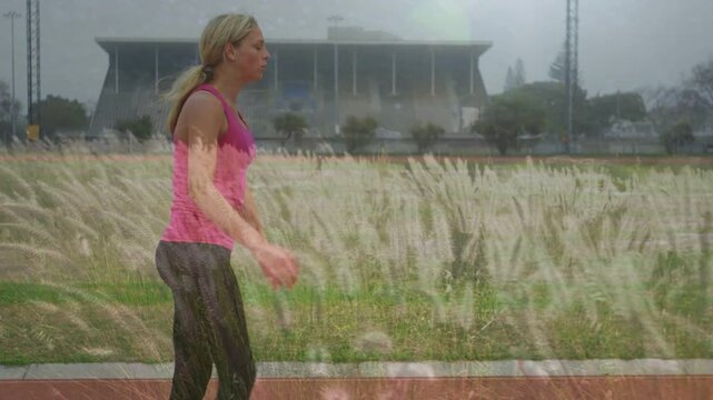 Girl warming up on track, swinging leg, balancing with grass overlaying her for training