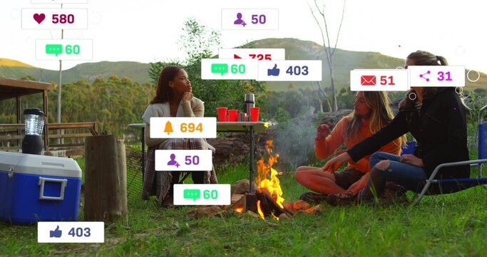 Gathering three friends wearing scarf and orange top around campfire at campsite, cooler, icons