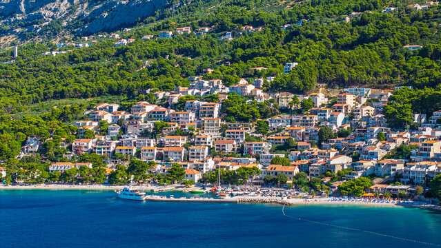 Scenic view of the coastal town of Brela on the Makarska Riviera in Croatia featuring Mediterranean houses with red roofs on a lush green hillside overlooking the blue Adriatic Sea