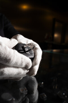 White gloves examining silver ring with gemstones for quality control.