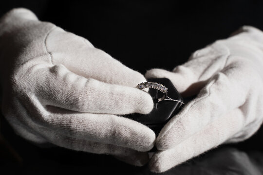 Jeweler inspecting silver ring with gemstones using white gloves in workshop.