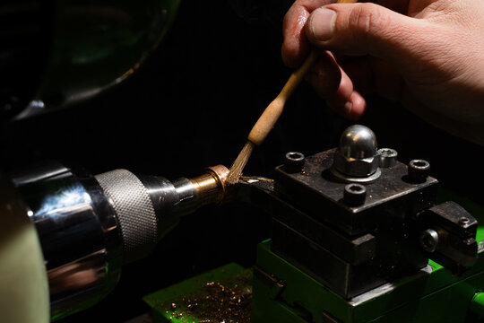 Jeweler applies cutting fluid with a brush before milling a ring on a precision machine.