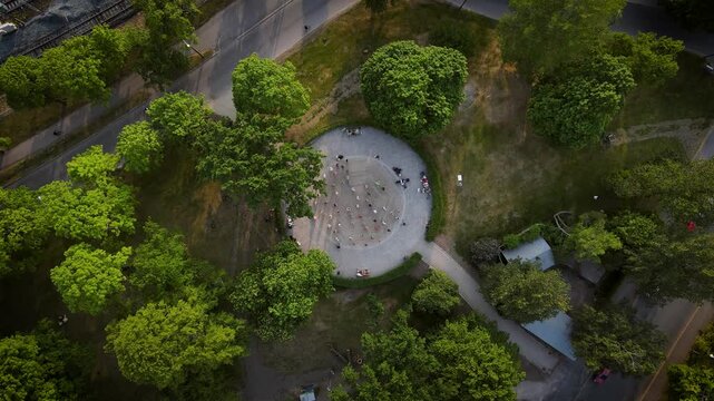 Cinematic aerial drone footage of Kaisaniemi Park dance pavilion on a beautiful sunny day. People enjoying outdoor dancing in a lively park atmosphere surrounded by greenery in Helsinki, Finland.