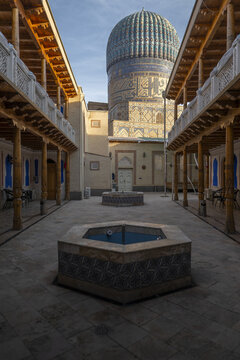 View of the Bibi-Khanym Mosque dome from a traditional courtyard with wooden columns and stone fountains in Samarkand, Samarqand Region, Uzbekistan.